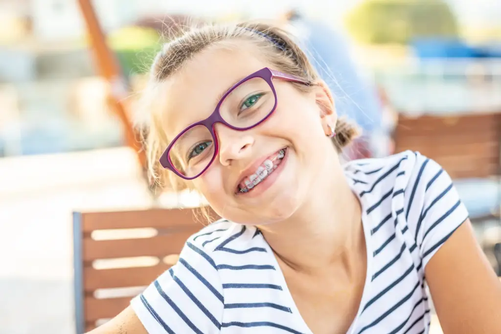 Smiling child with glasses showing healthy teeth after pediatric dental care