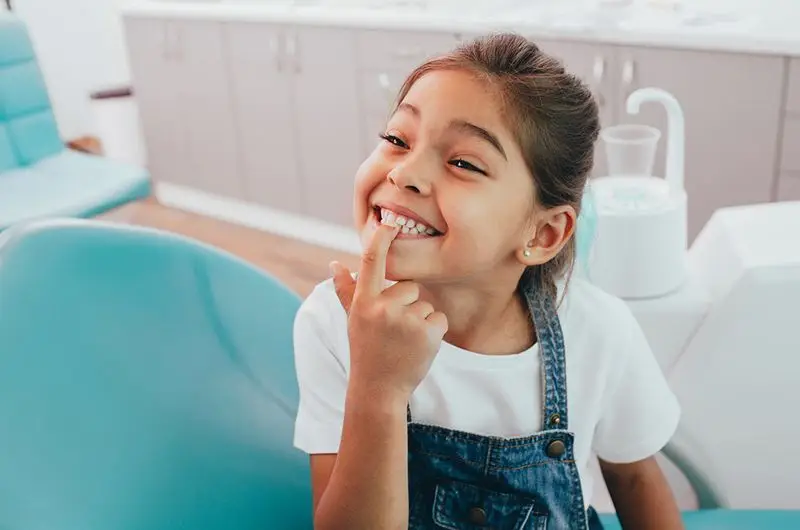 Child pointing to healthy teeth after dental checkup at pediatric dentist